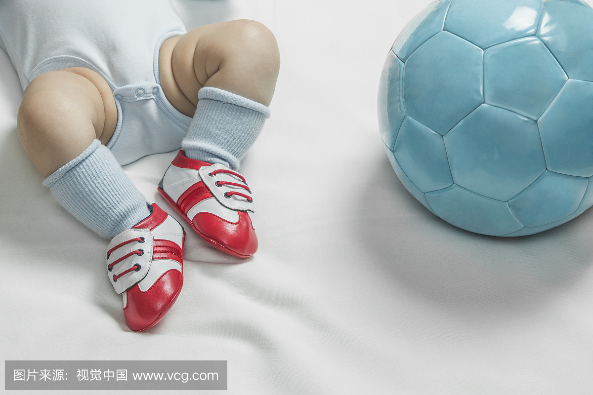 一个穿着婴儿足球鞋的男婴躺在一个足球旁边