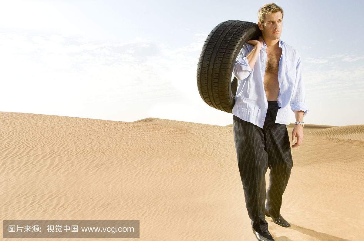 A man standing in the desert with a tyre
