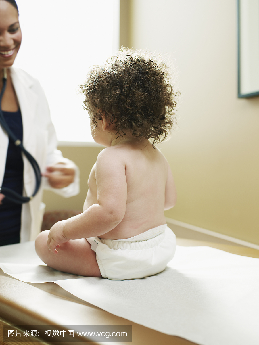 女医生与婴儿患者(11个月)坐在检查台上,后视图