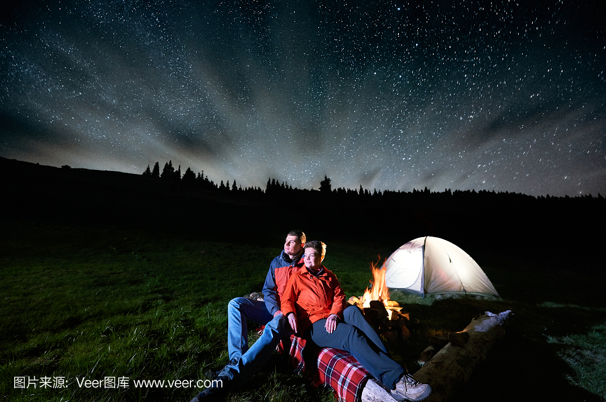 夜间露营在山上。浪漫的情侣游客坐在篝火附近