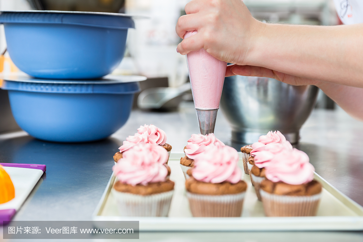 妇女在糕点面包店作为糖果上釉与结冰袋松饼