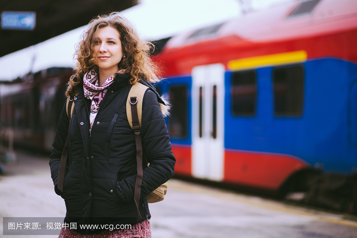 等待火车的愉快的卷曲的头发的女孩在火车站