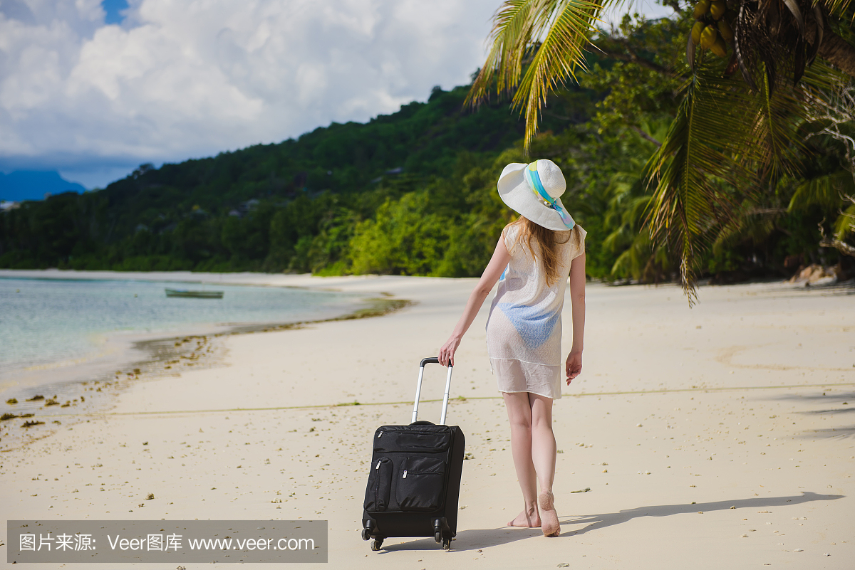 有一个手提箱在一个热带海滩的女人。