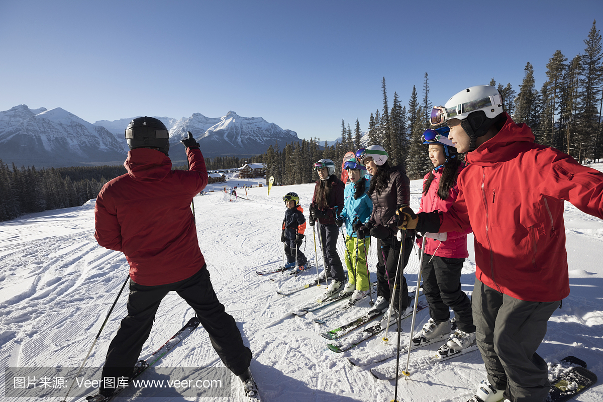 家庭从滑雪胜地教练接受组滑雪课在阳光明媚的