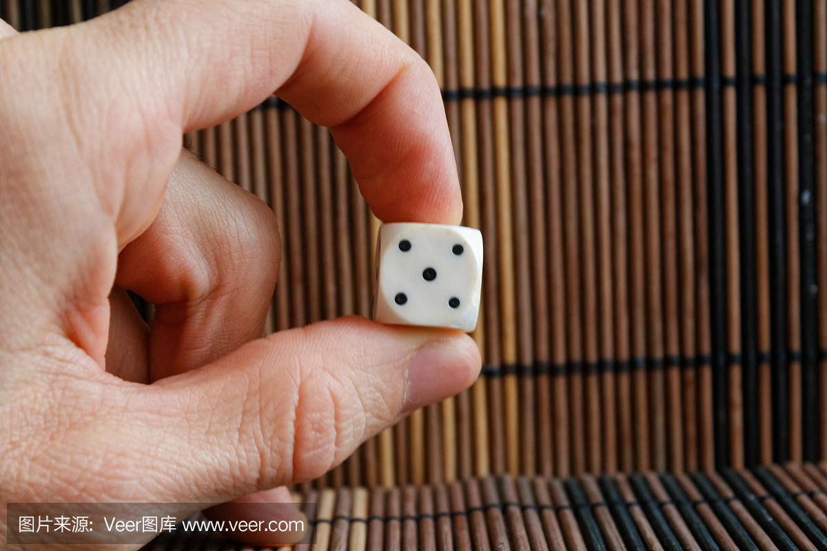 一个白色塑料骰子在棕色木桌背景的人的手中。