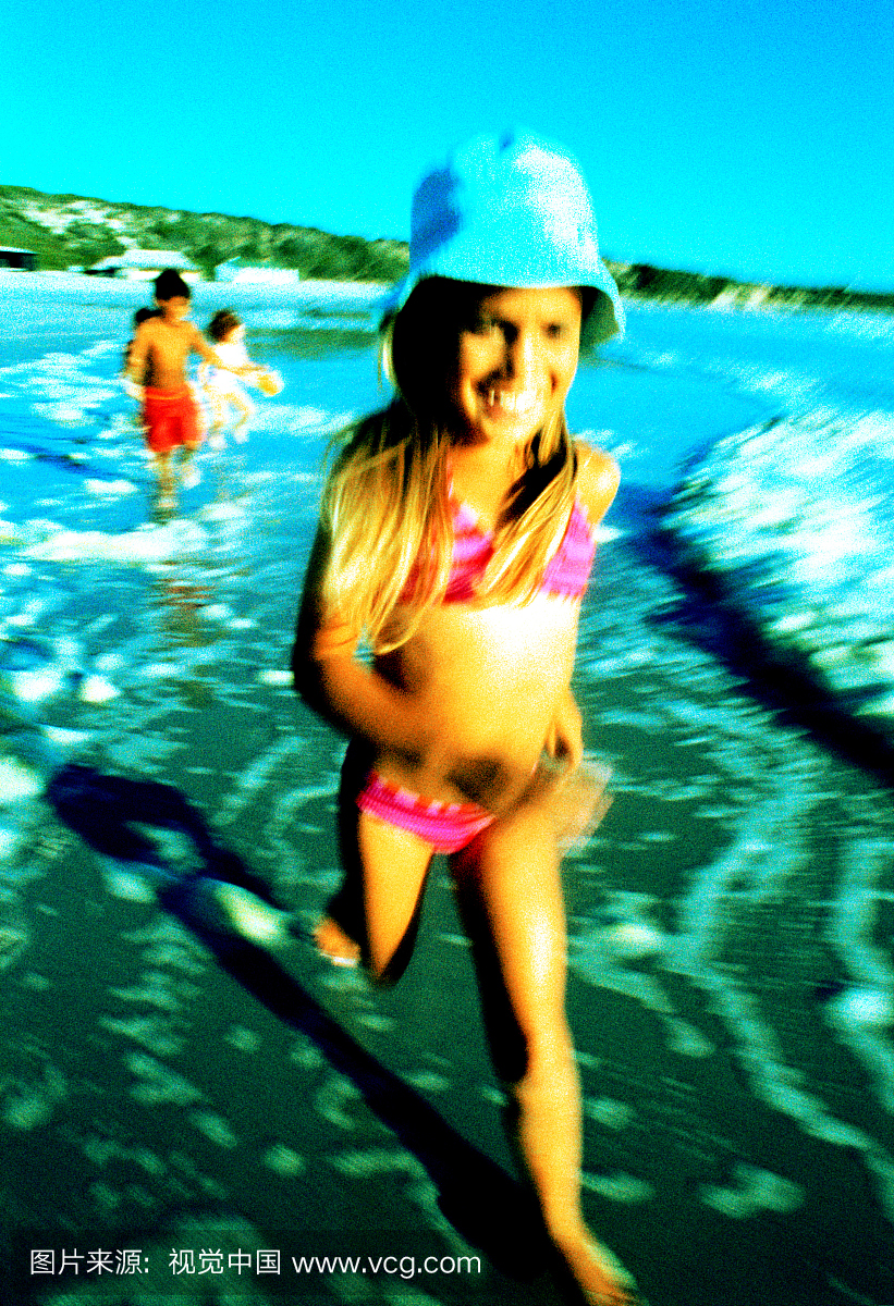 年轻的女孩(6-8岁)穿着比基尼和sunhat在沙滩上