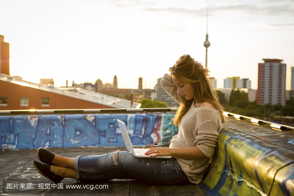 年轻女子坐在屋顶上,在笔记本电脑上工作 - 背光