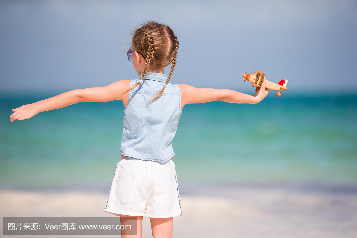 快乐的孩子女孩玩玩具飞机在海滩上。孩子梦想