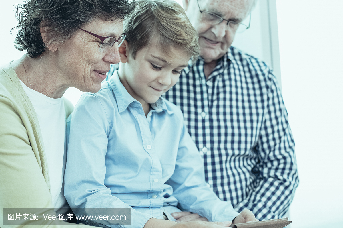 现代男孩与祖父母使用平板电脑。他们一起看教