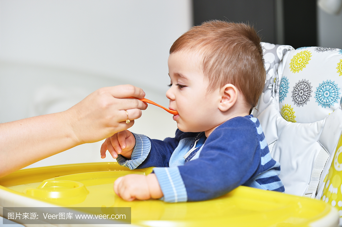 男婴在婴儿椅上用勺子吃