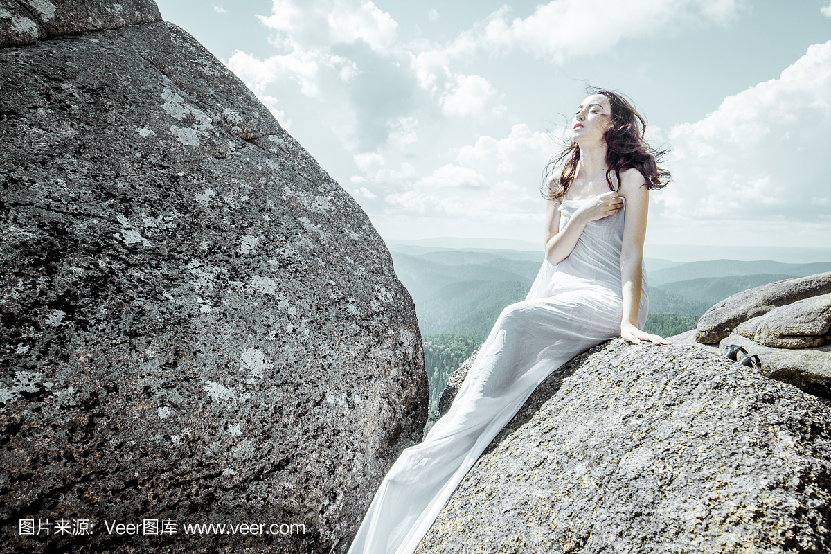 白色长布裙下的女孩在夏天的大岩石上