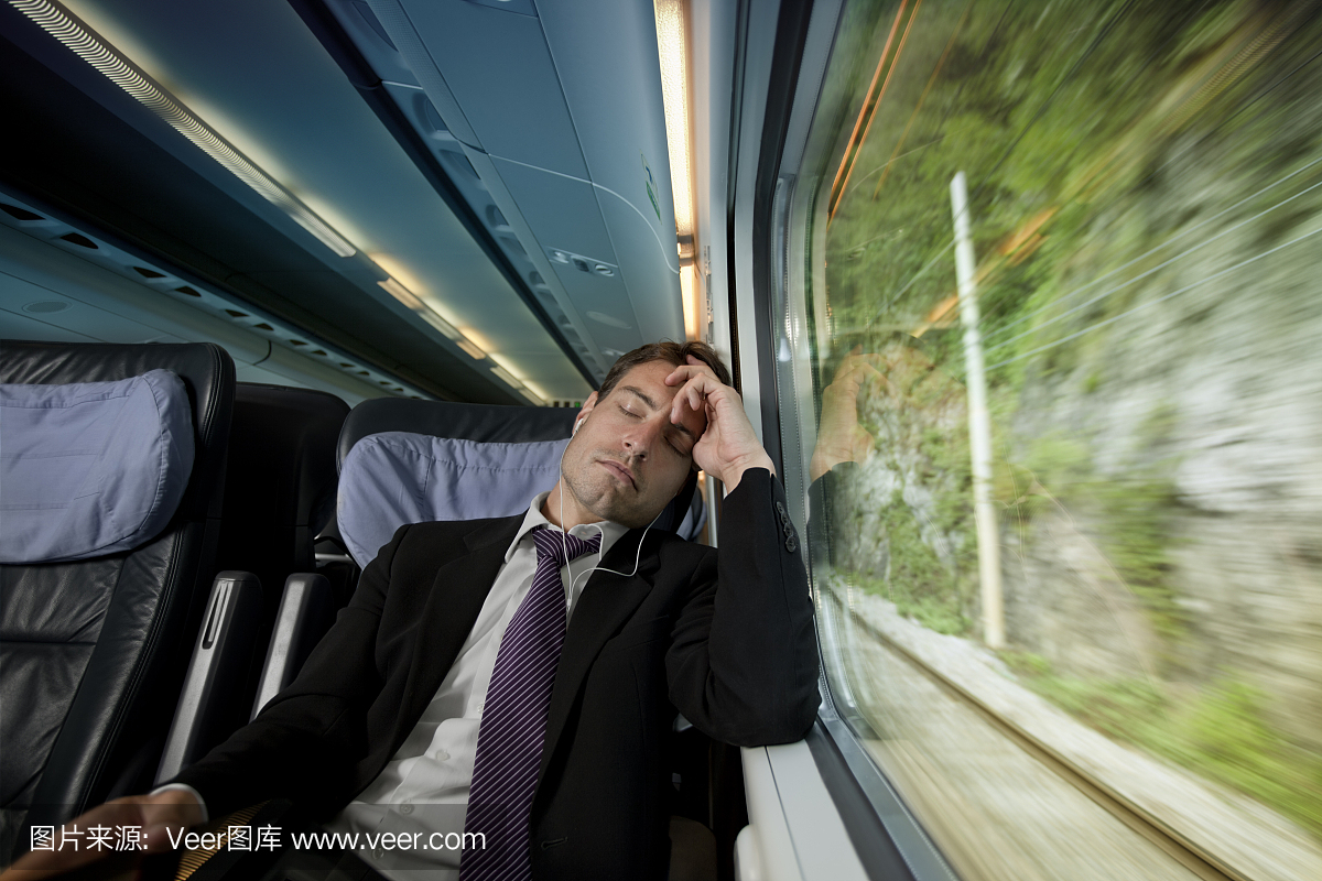 过度劳累的商人在火车上的窗户旁边睡觉和听音