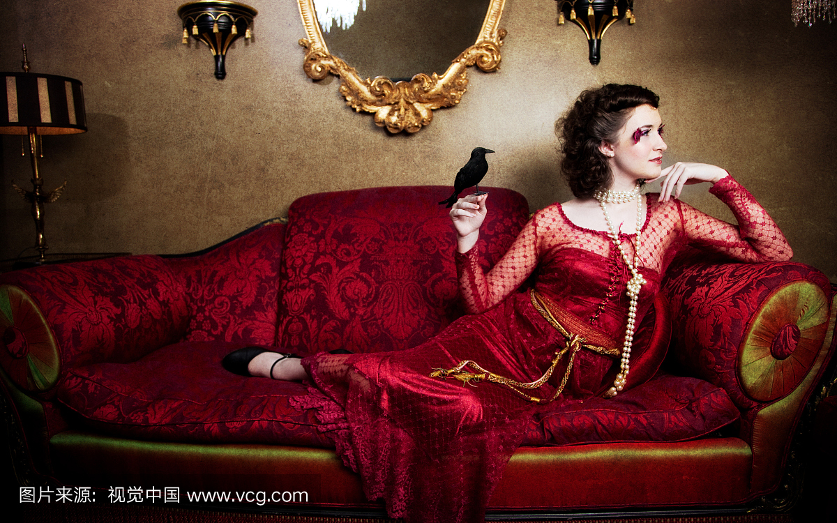 红色仿古沙发上的美丽的女人与黑鸟
