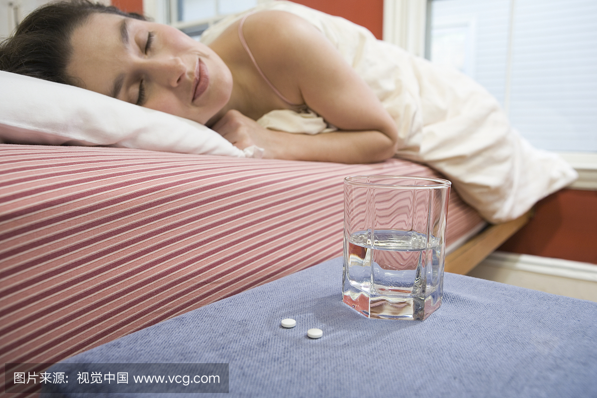 睡在床上的女人用药丸和她旁边的水玻璃