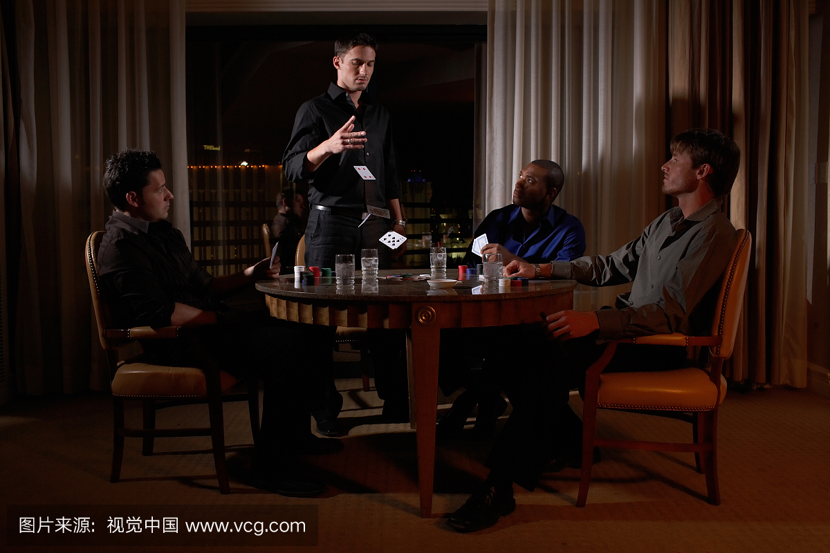 四人坐在圆桌上黑暗的酒店房间玩纸牌,一个人