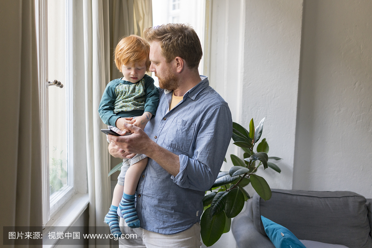 Father holding toddler son using mobile phone