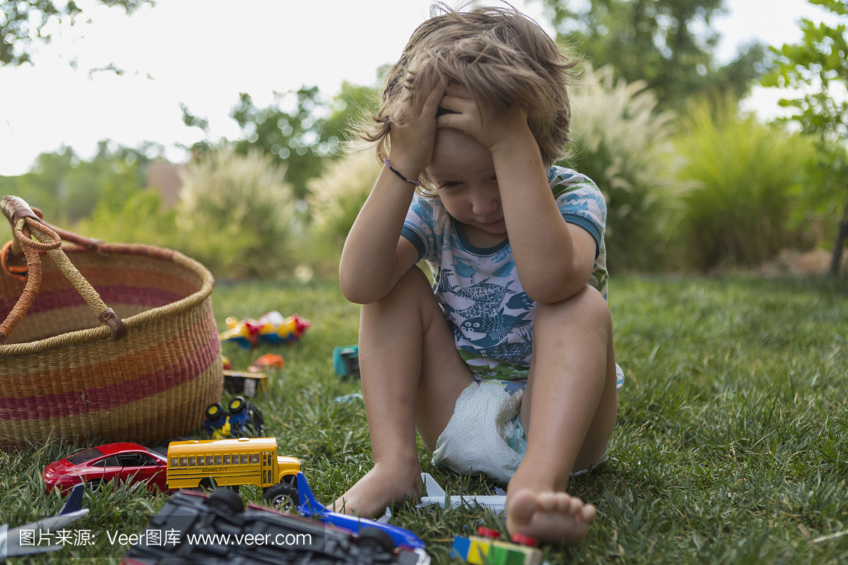 沮丧的3岁男孩玩玩具篮子的绿色草坪上