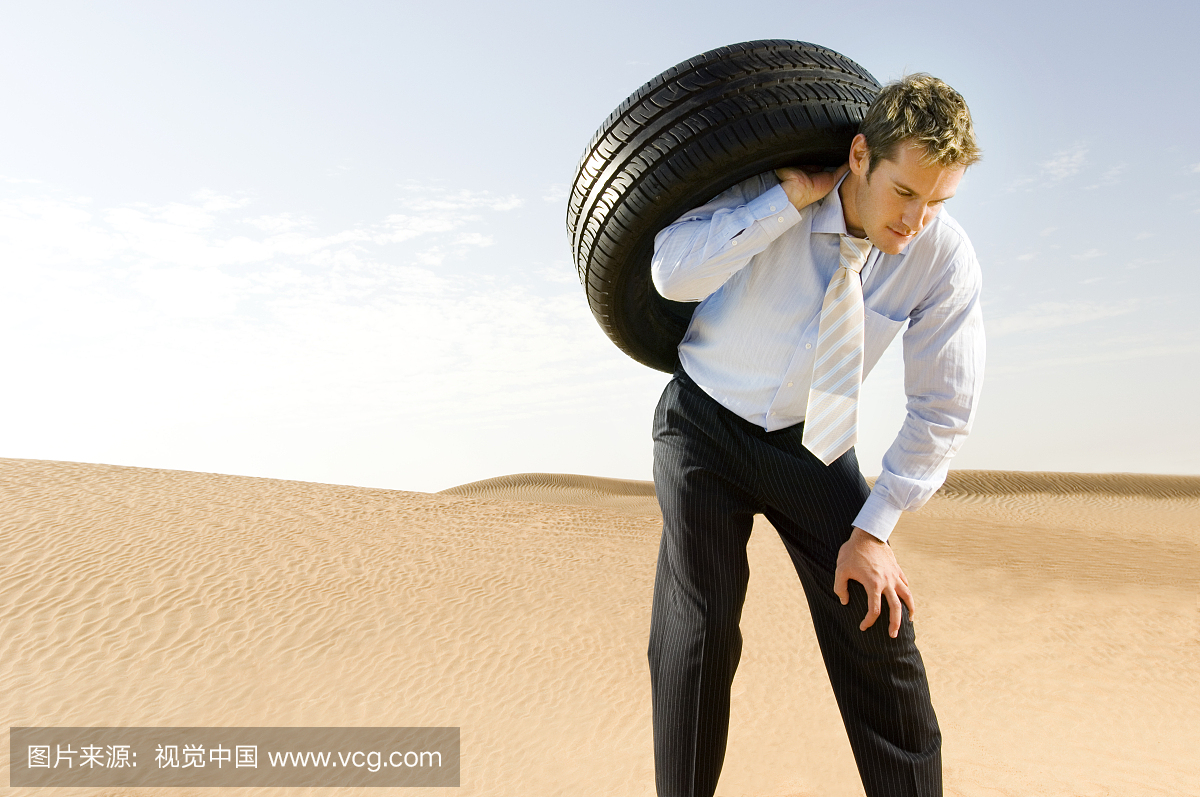 A man standing in the desert with a tyre