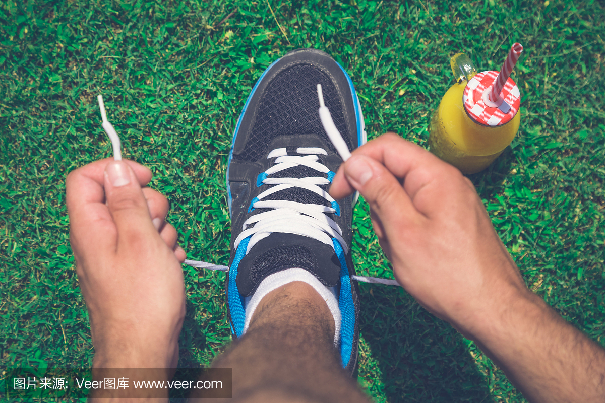 Man runner tying shoe laces on grass and glass