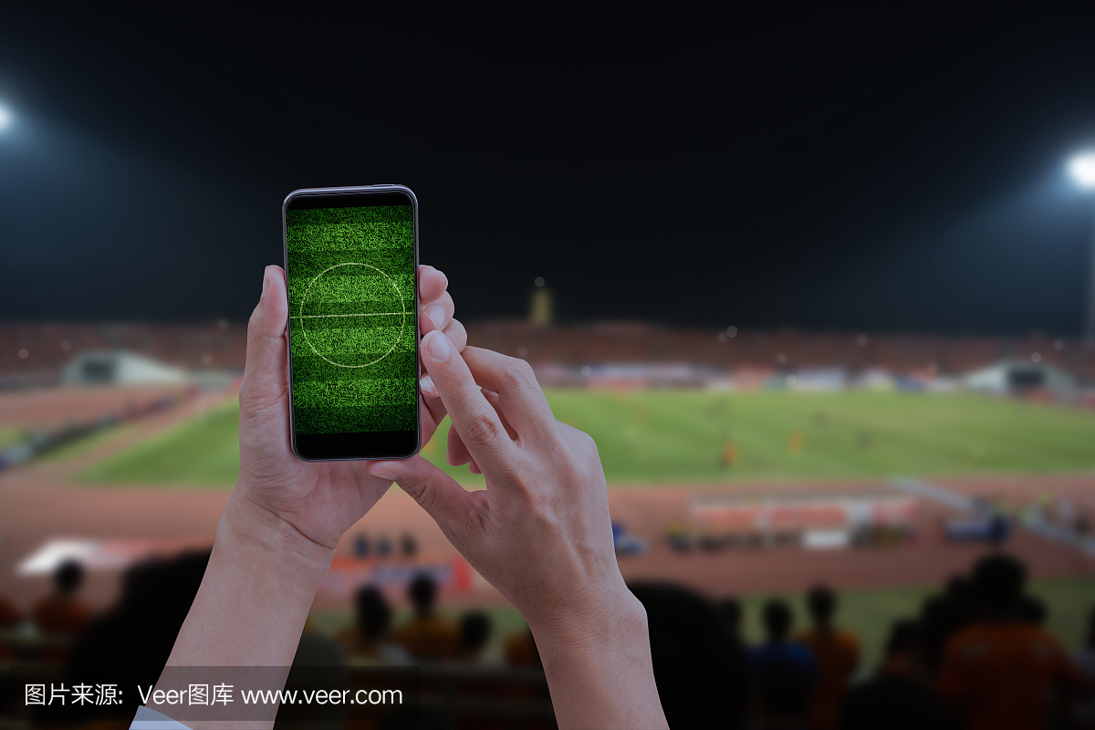 手持手机智能手机与足球场,模糊的社会