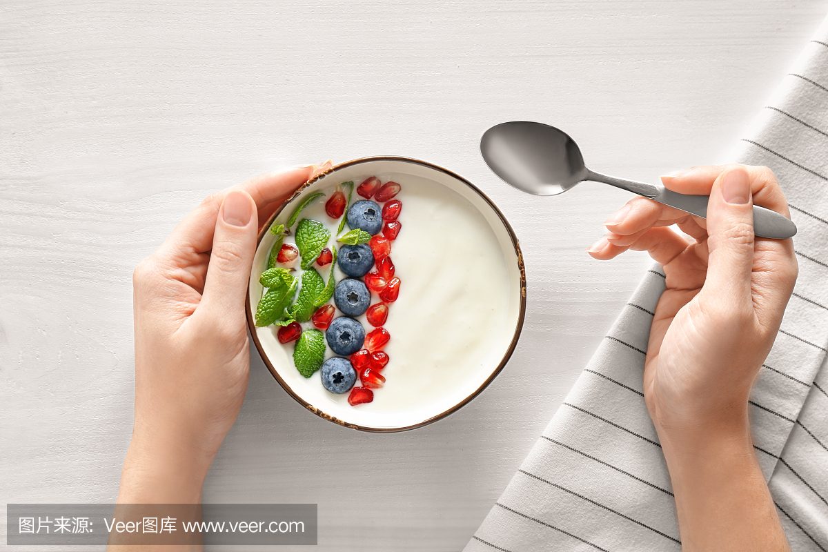 女人吃美味酸奶配蓝莓和石榴籽在木桌上