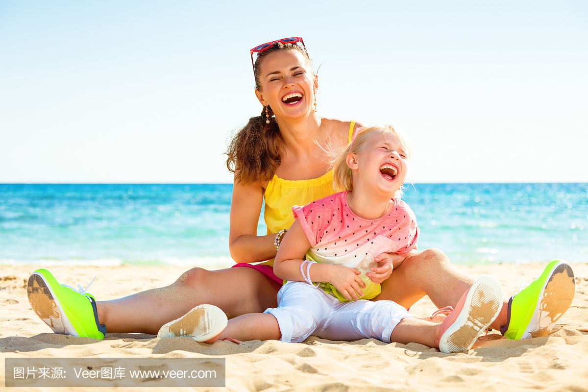 微笑时髦的母亲和女儿在海边玩得开心