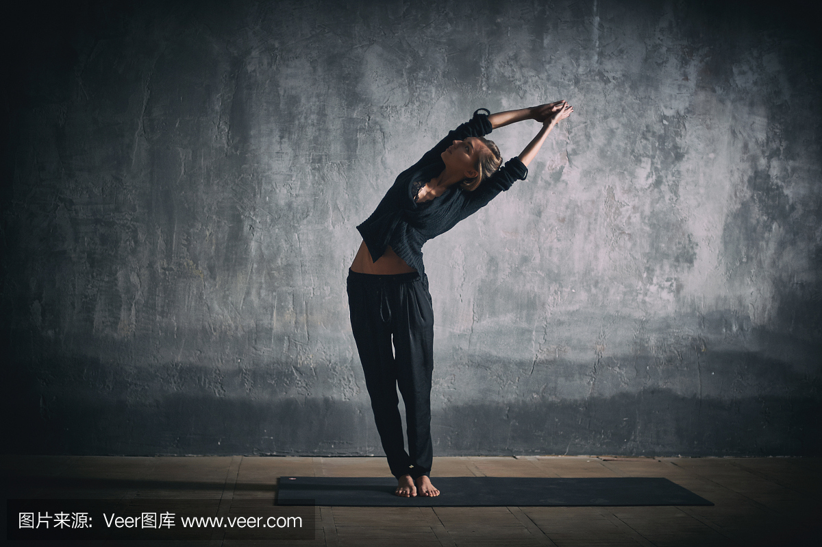 美丽的女人练习瑜伽体式Tiriaka Tadasana在黑