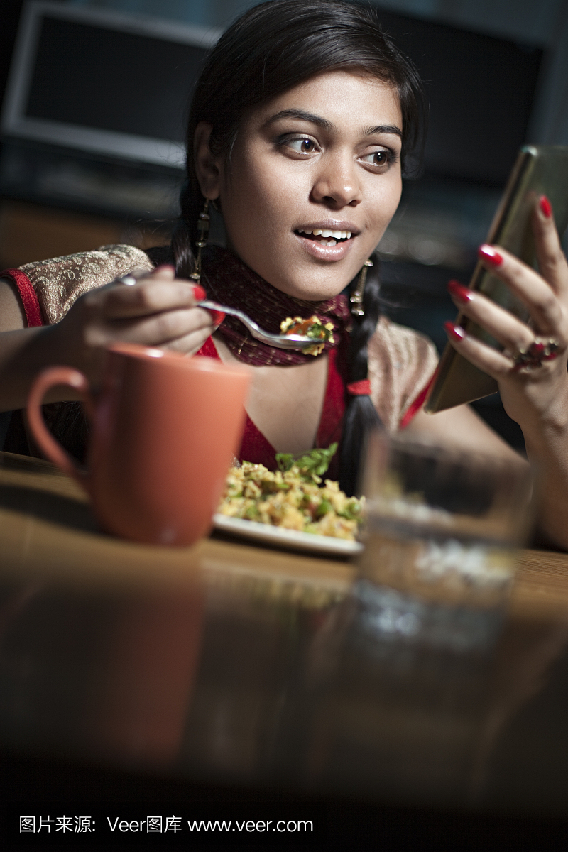漂亮的印度女子吃点心咖啡和使用智能手机。