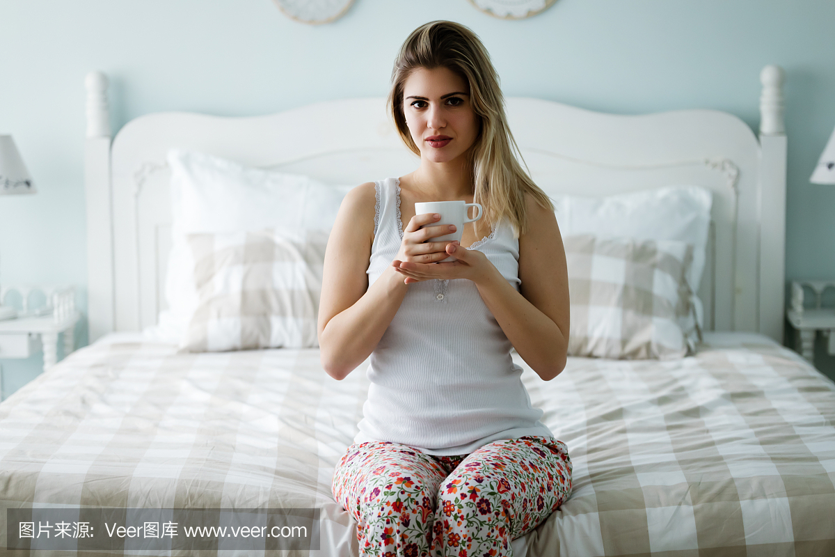 美丽的女人早晨喝咖啡坐在床上