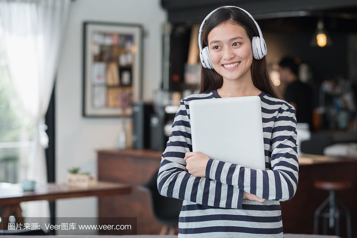 亚洲十几岁的女孩拥抱笔记本电脑和听音乐与快