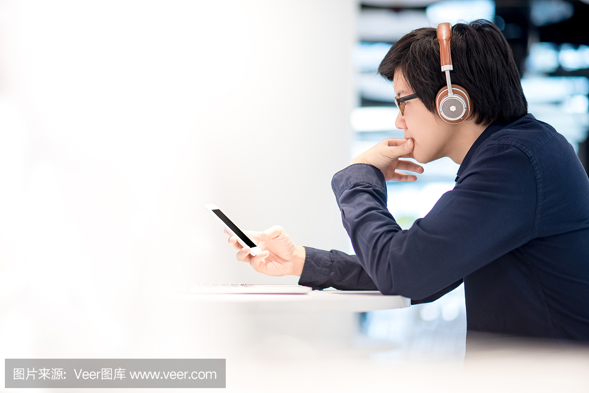 听音乐的年轻亚裔商人由耳机和智能手机,当与