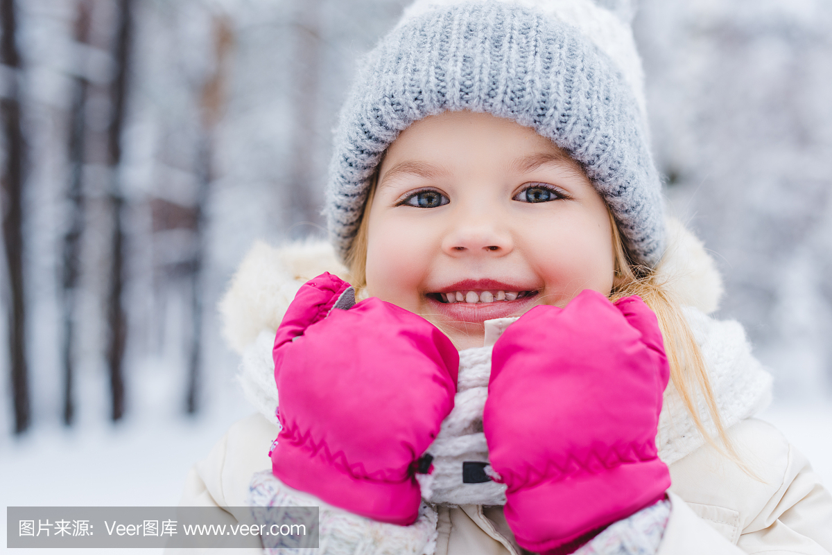 可爱的小女孩,戴着帽子和手套微笑在冬季公园