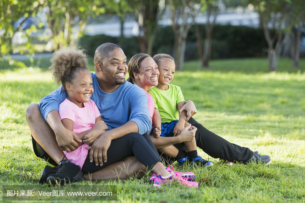 快乐的黑人家庭四人坐在公园的草地上
