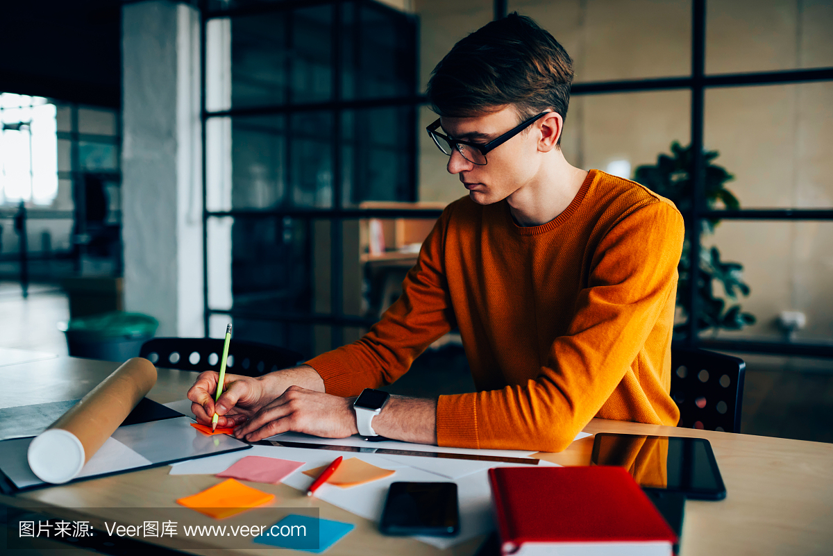 沉思的男性工程师起草坐在工作场所与设备做笔