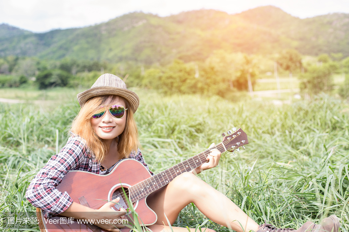 年轻的时髦女孩坐在弹吉他和唱歌。