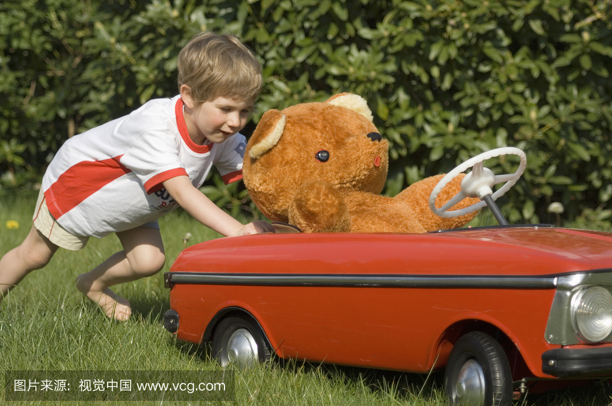 男孩(3-4岁)把玩具车推在草地上