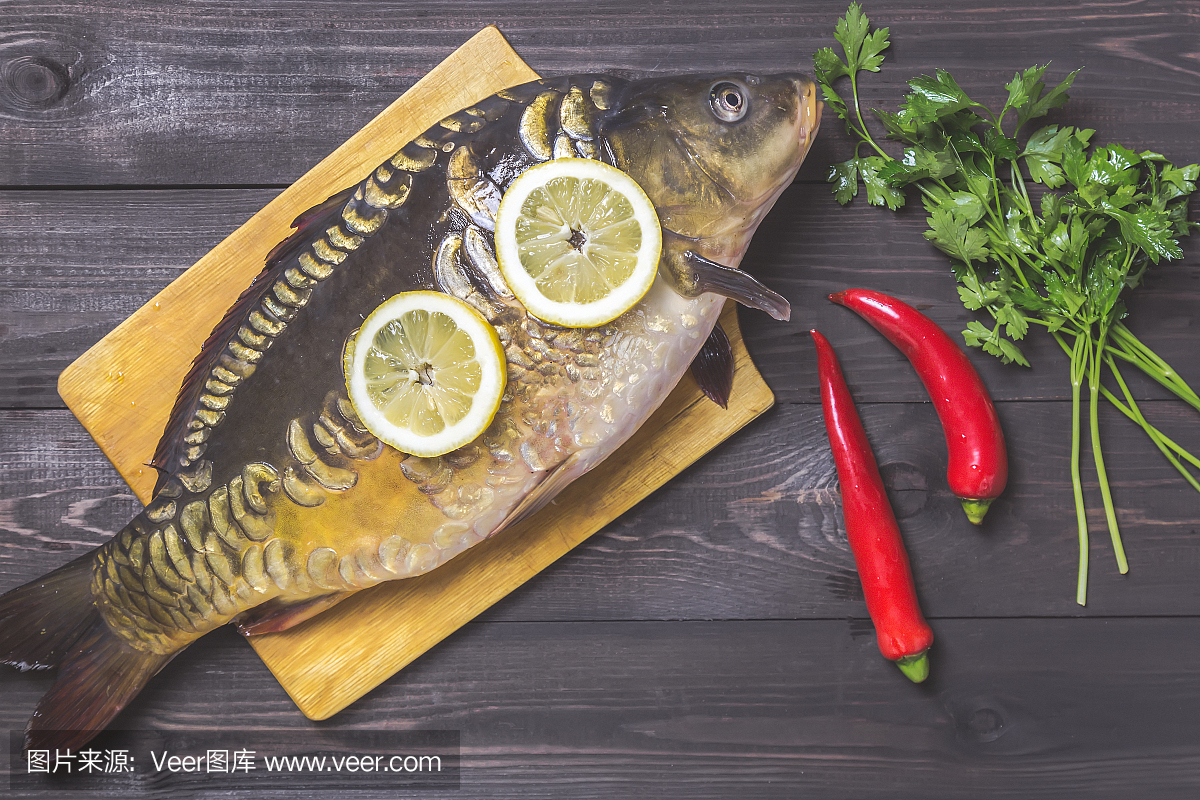 镜子鲤鱼河鱼与柠檬,草药和胡椒在黑木桌上