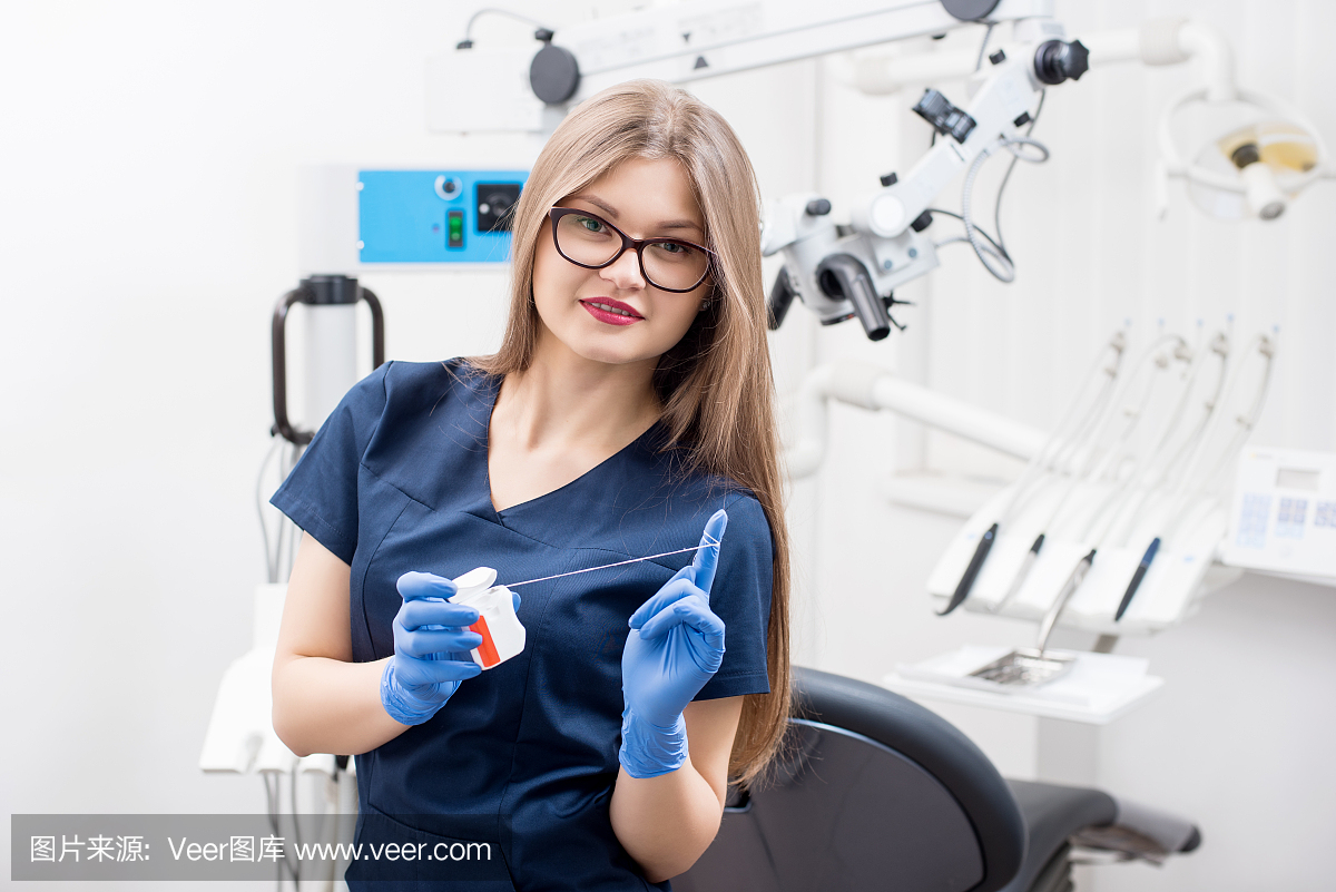 年轻人微笑女牙医用牙线在牙科诊所的肖像。医