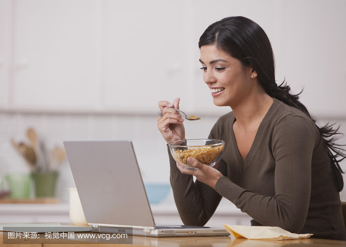 西班牙裔美国人吃早餐谷物,看笔记本电脑
