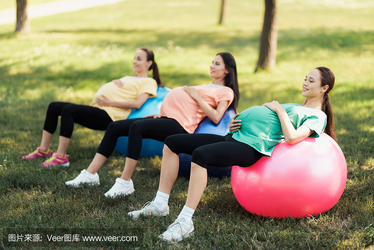 三名孕妇躺在公园里的瑜伽球上。他们抱着他们