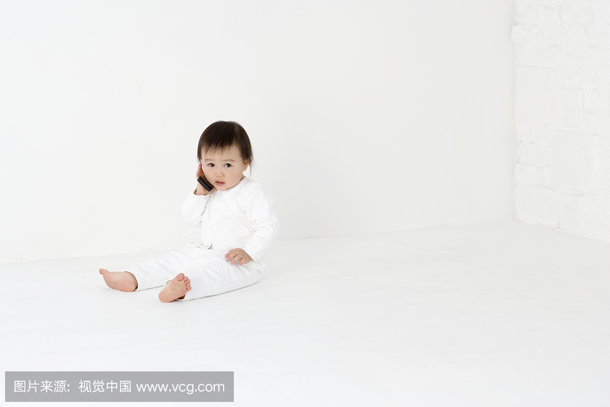 女婴(15-18个月)坐在工作室的地板上,在手机上