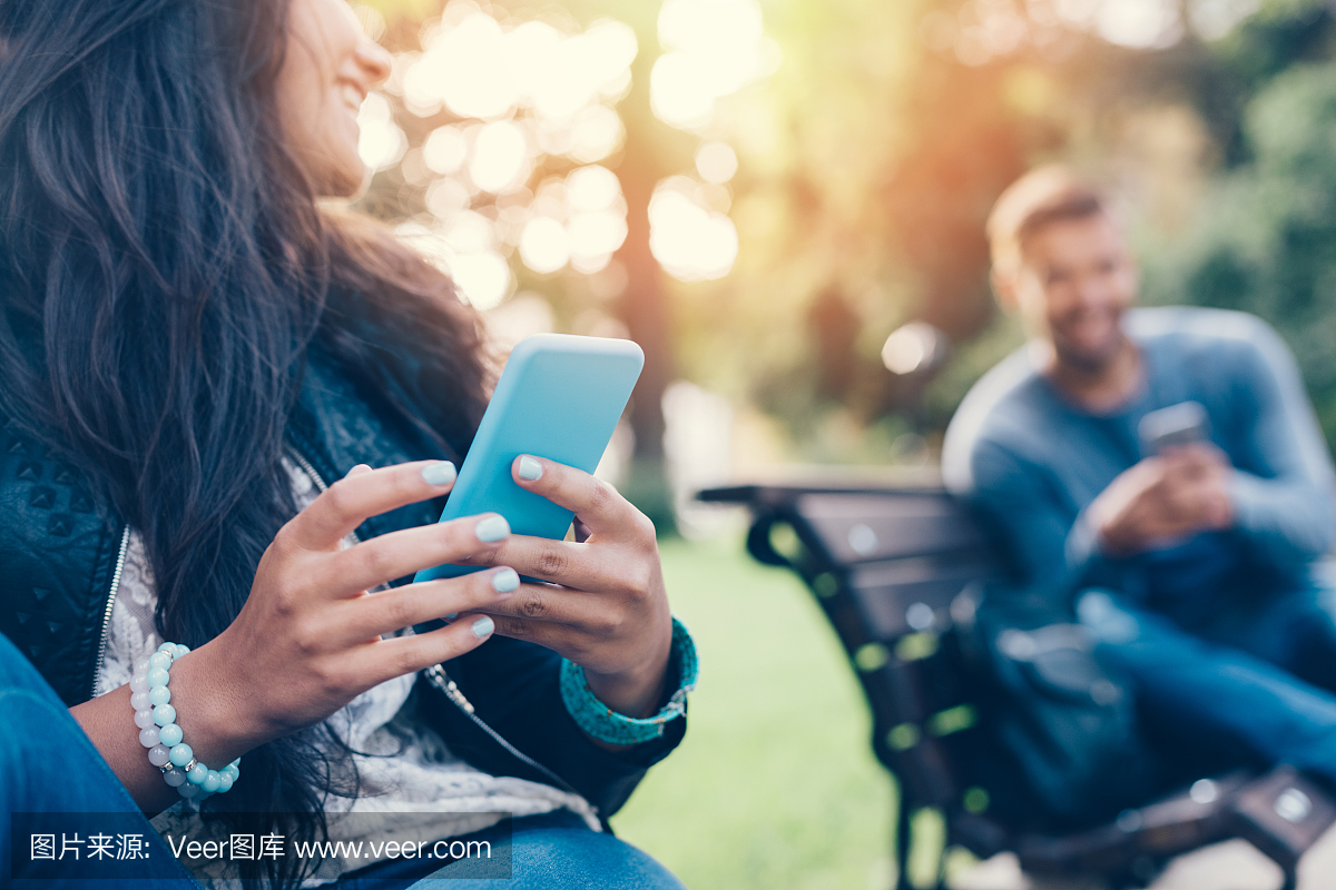 在公园里调情的夫妇在智能手机上发短信