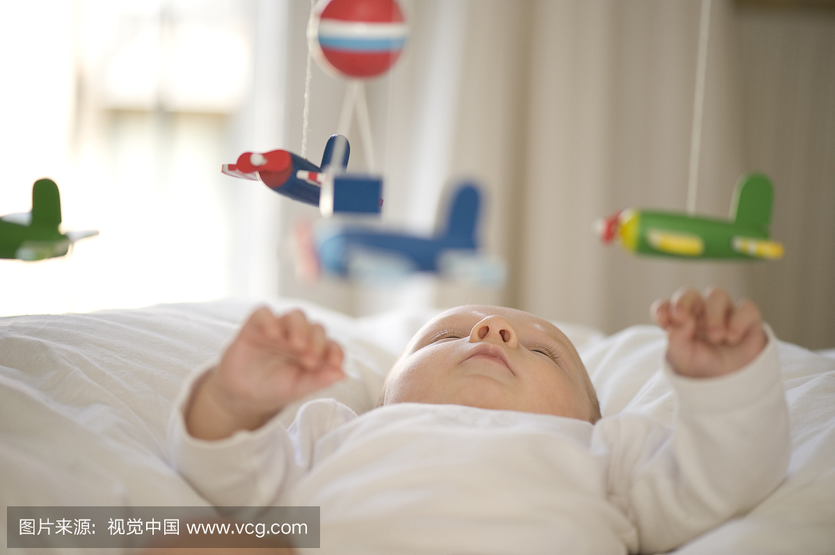 男婴2个月,在婴儿床上看着玩具飞机的手机