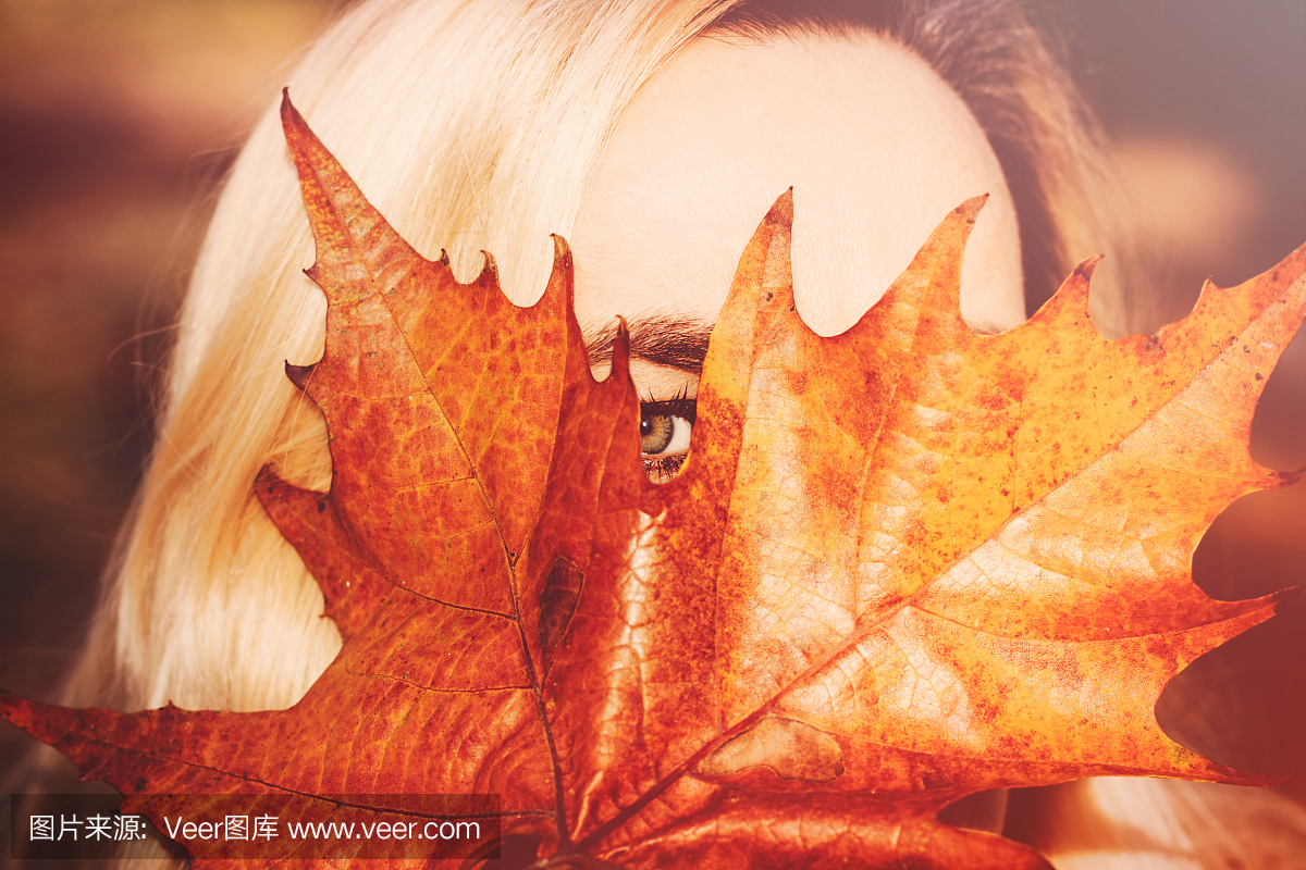 有绿色的眼睛的金发碧眼的女人用叶子遮住她的