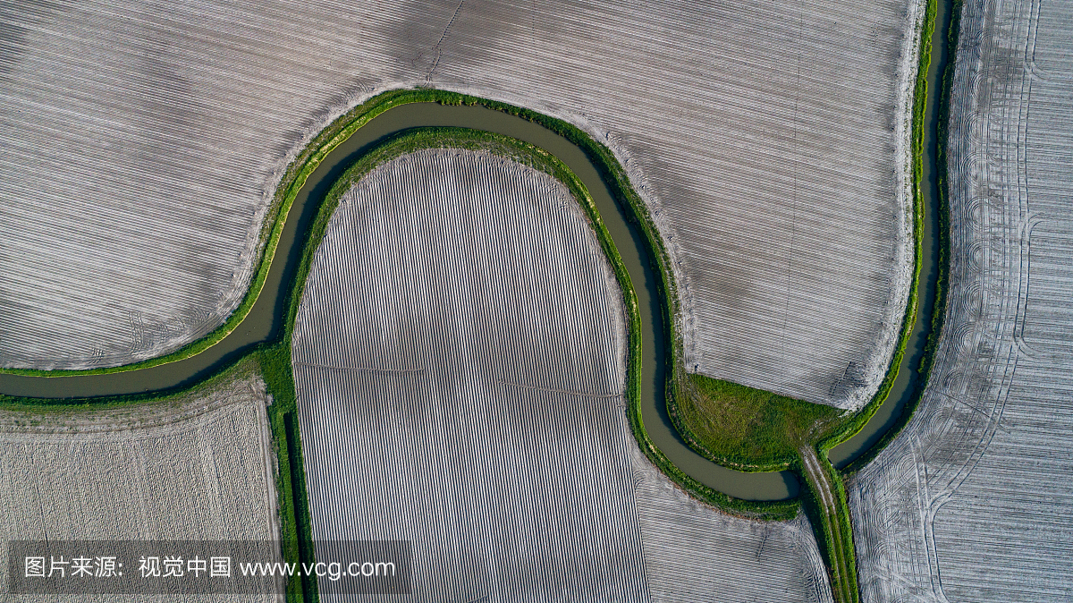 Aerial view of a river flowing through ploughed f