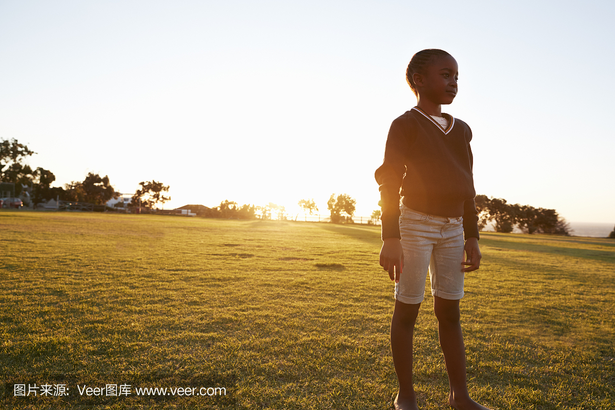 站在日落时的公园的非洲小学女孩
