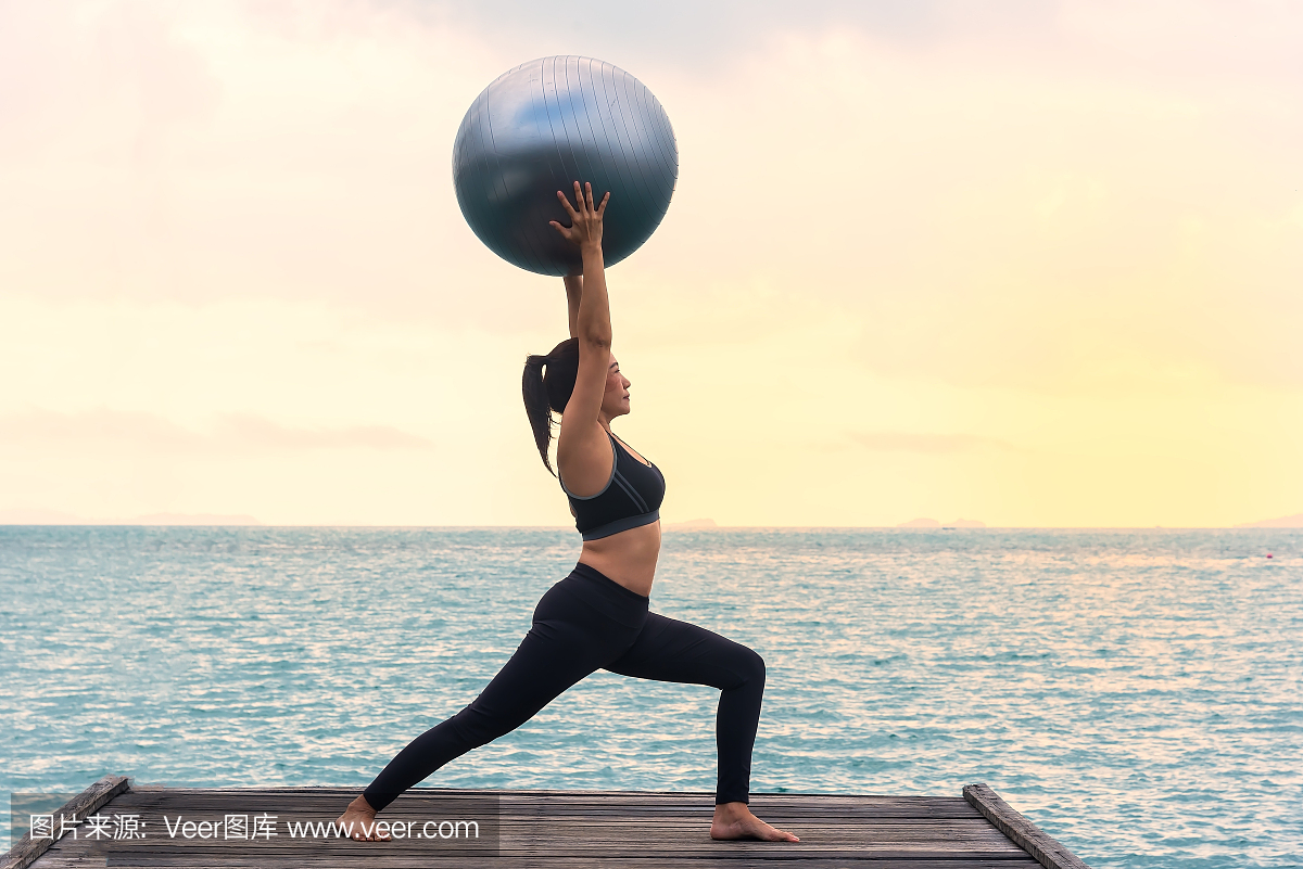 瑜伽球,普拉提健身球年轻女子在海滩日出背景