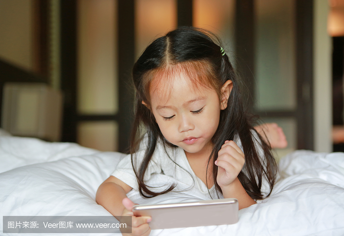 可爱的小女孩在床上看手机。
