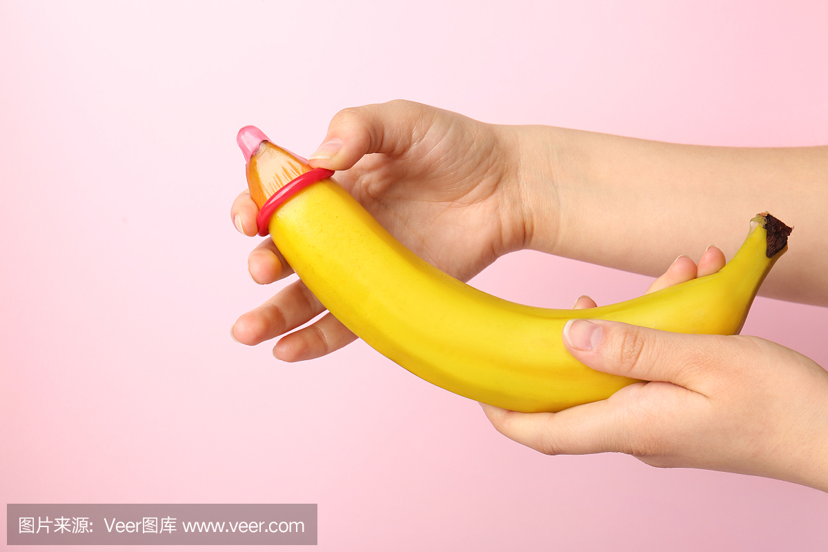 将避孕套放在香蕉上的女人反对颜色背景。安全