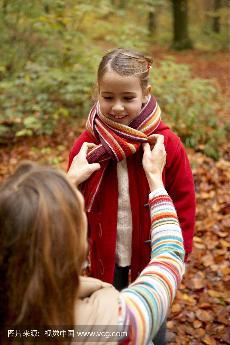 母亲在秋天的森林里用她的女儿脖子上的围巾围